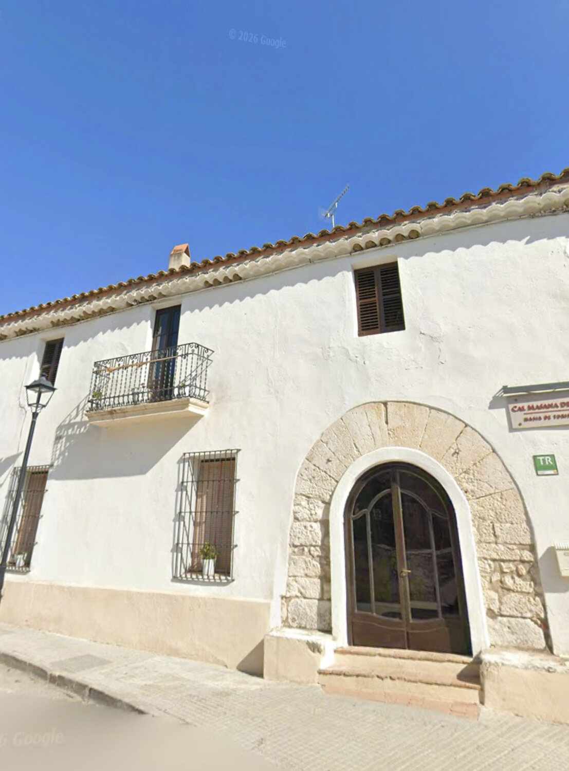 The whitewashed village house with its stone arched doorway under a clear blue sky