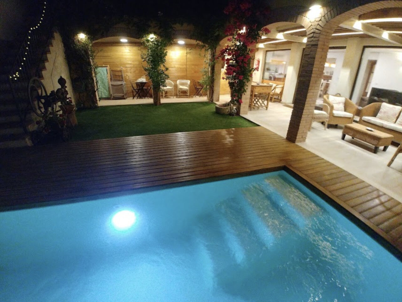 The pool and arcade at night under string lights and bougainvillea
