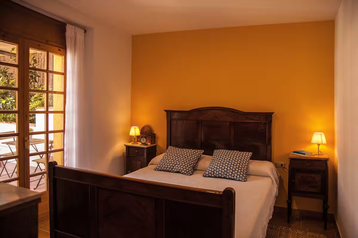 A double bedroom with warm wooden beams, linen bedding and a reading lamp