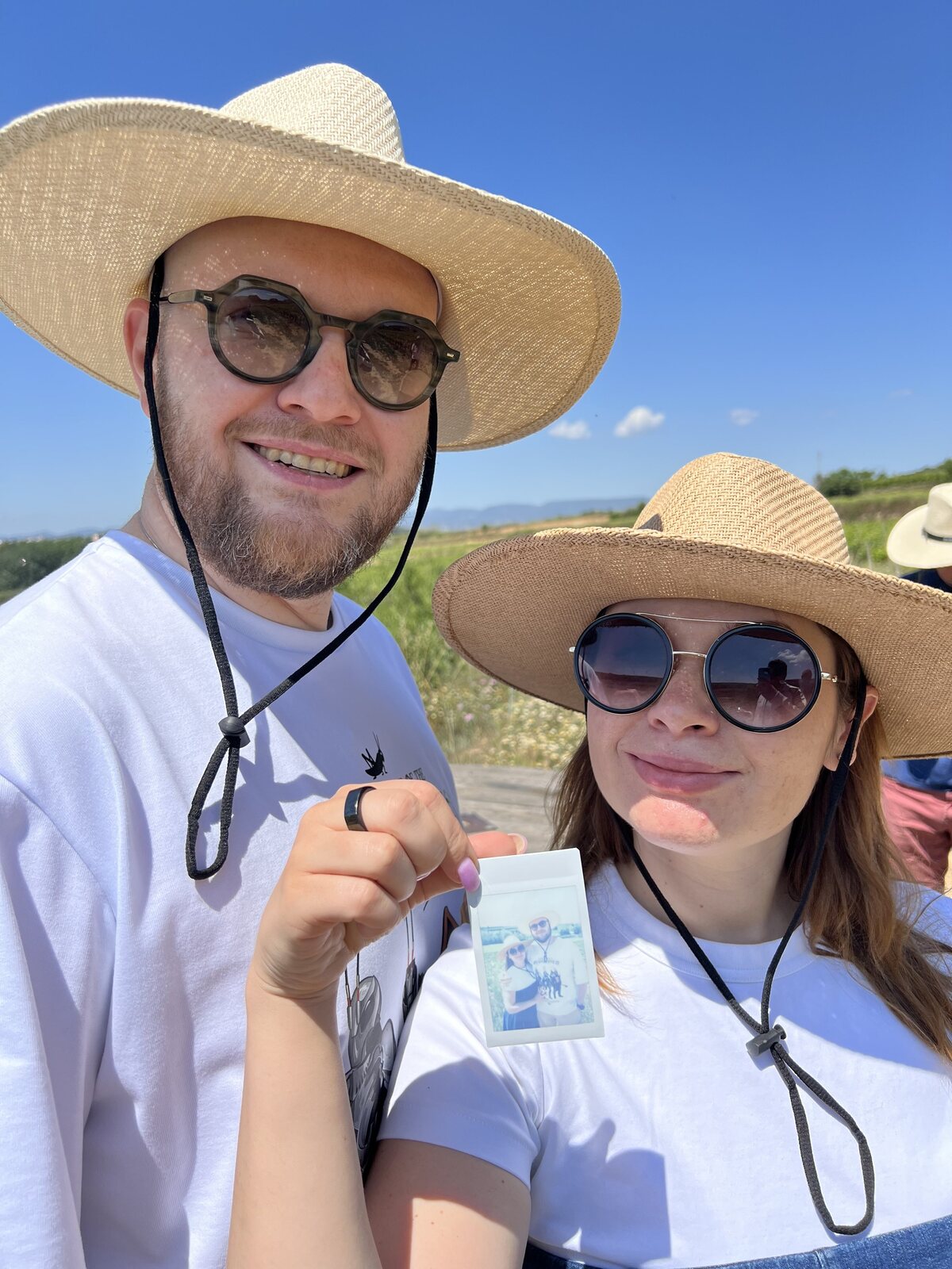 Two guests in straw hats walking between the vines under a blue sky