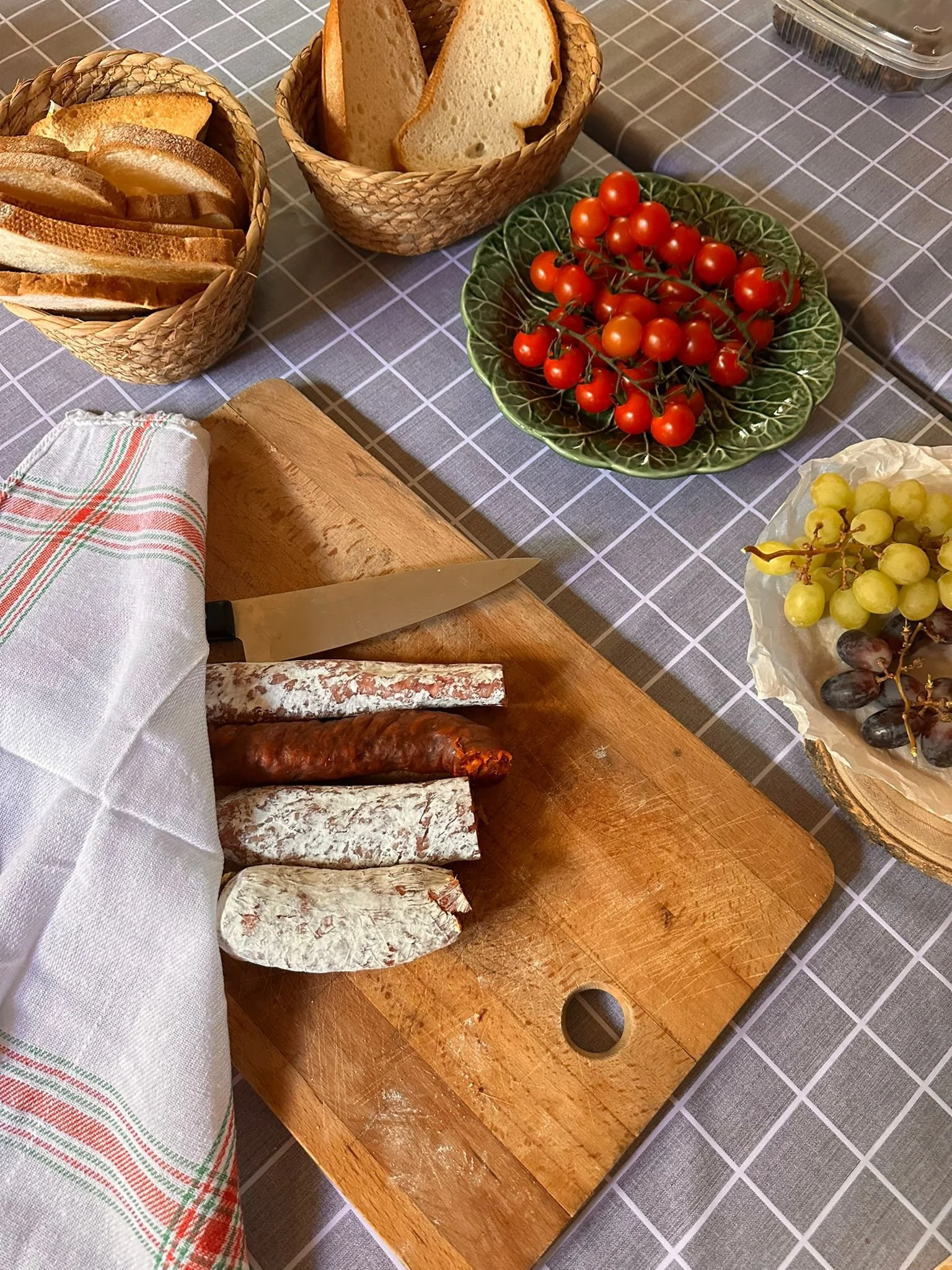 A board of bread, tomatoes, cured meat and grapes